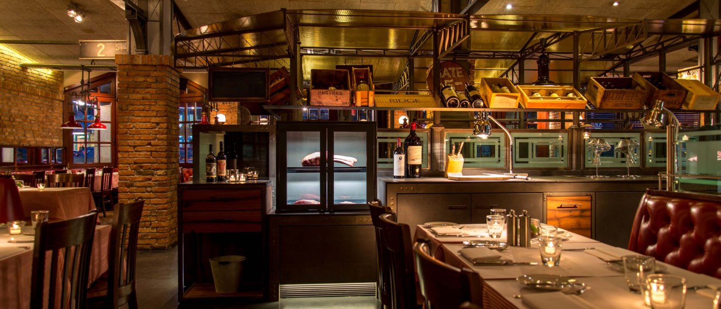 Stilvolles Restaurant mit Ziegelwänden, gedeckten Tischen und Weinregalen. Warmes Licht schafft eine gemütliche Atmosphäre., © Pier 51 Stilvolles Restaurant mit Ziegelwänden, gedeckten Tischen und Weinregalen. Warmes Licht schafft eine gemütliche Atmosphäre., © Pier 51