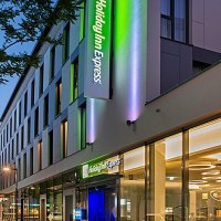 Außenansicht eines modernen Holiday Inn Express Hotels bei Dämmerung, mit beleuchtetem Logo und Glasfassade., © Holiday Inn Express Waiblingen Außenansicht eines modernen Holiday Inn Express Hotels bei Dämmerung, mit beleuchtetem Logo und Glasfassade., © Holiday Inn Express Waiblingen