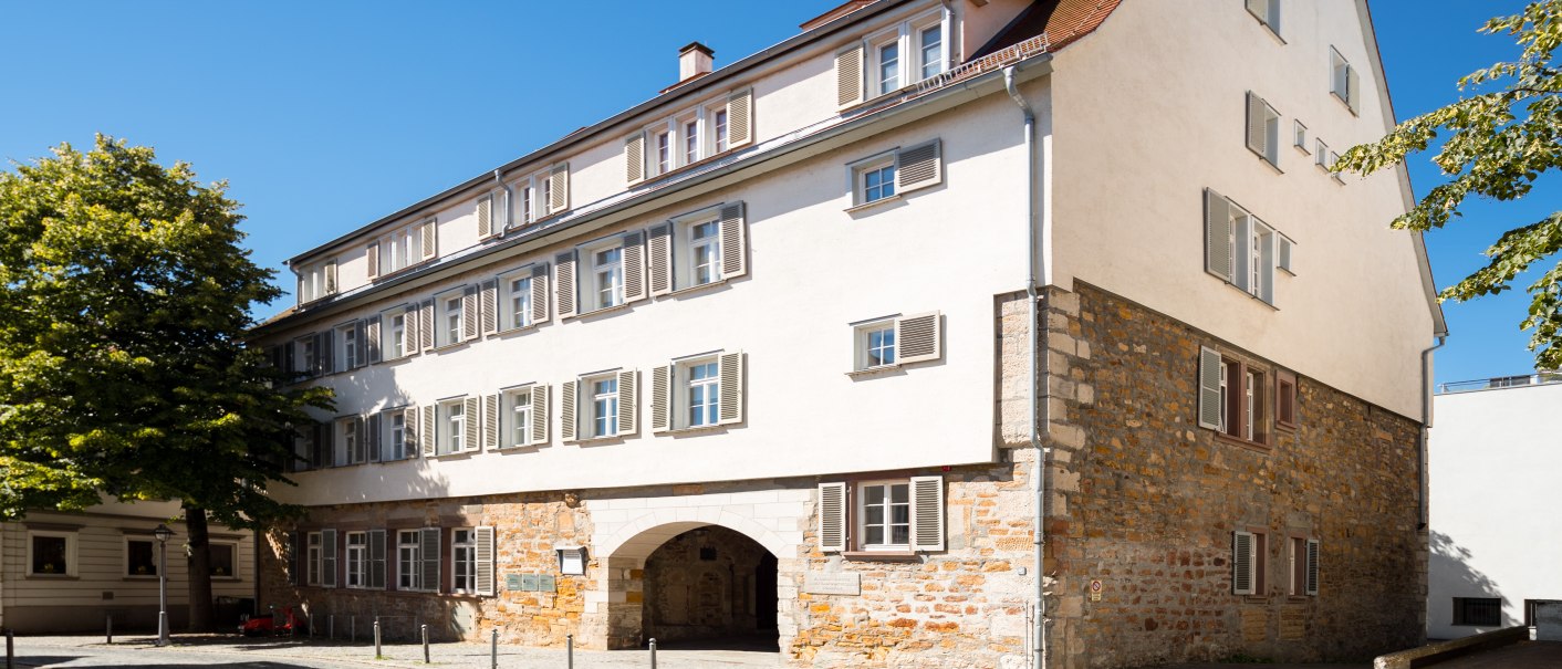 Historisches Gebäude mit Steinmauer und weißen Fensterläden, umgeben von Bäumen, unter blauem Himmel in Göppingen., © Stadtmarketing Göppingen