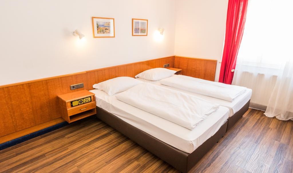 Ein Doppelzimmer mit zwei Einzelbetten, Holzboden, roten Vorhängen und zwei Bildern an der Wand., © ARNOTEL GmbH Ein Doppelzimmer mit zwei Einzelbetten, Holzboden, roten Vorhängen und zwei Bildern an der Wand., © ARNOTEL GmbH