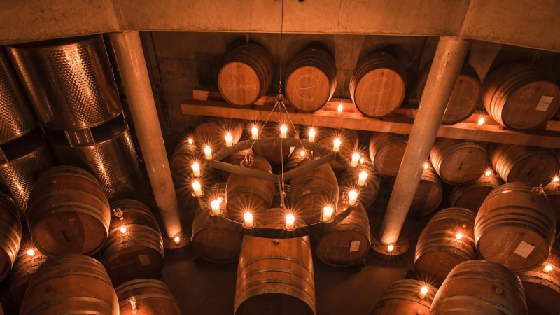 Weinkeller mit Holzf&auml;ssern, warmem Licht und Kronleuchter; links das Logo &bdquo;SCHINATMANN&ldquo;., &copy; Weingut Schnaitmann