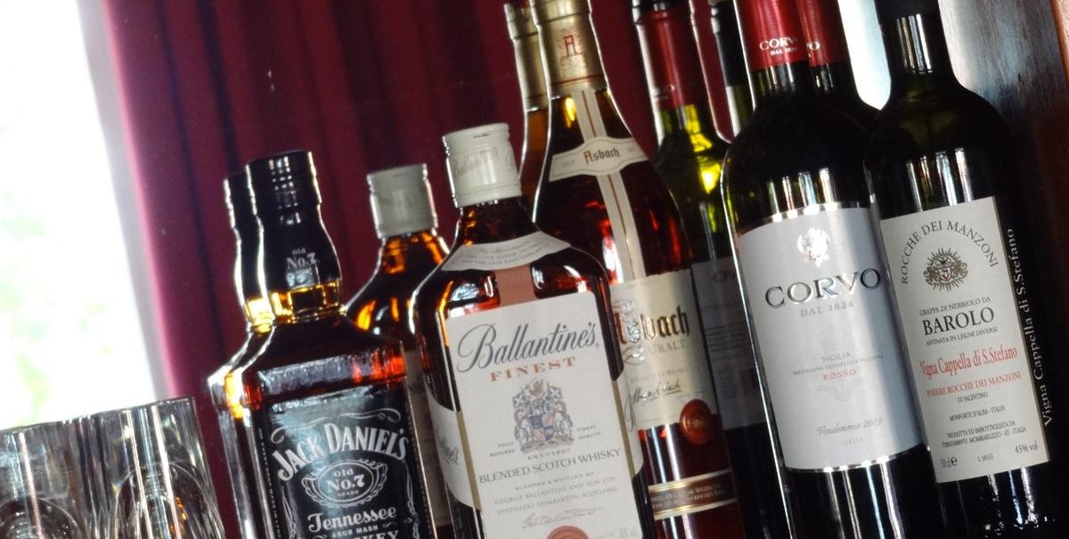 Verschiedene Whisky- und Weinflaschen stehen auf einem Regal vor einem roten Vorhang. Links sind Gläser zu sehen., © Hotel Arcis Verschiedene Whisky- und Weinflaschen stehen auf einem Regal vor einem roten Vorhang. Links sind Gläser zu sehen., © Hotel Arcis