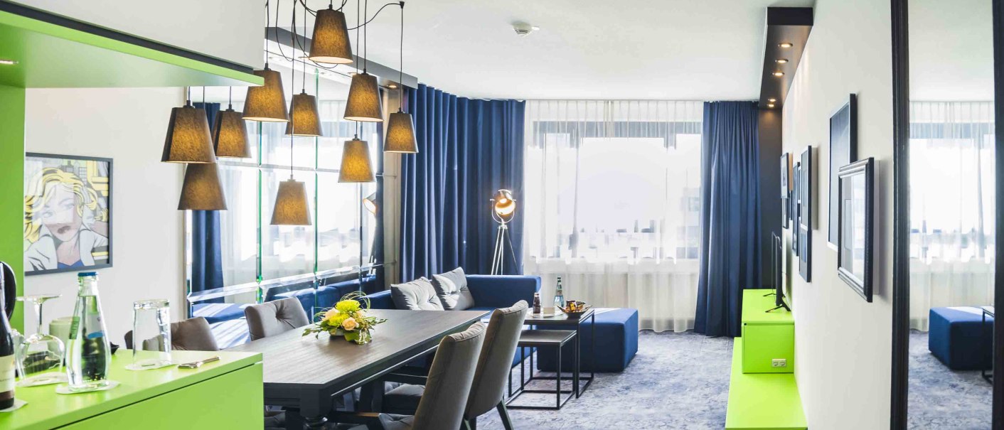 Moderne Suite mit Esstisch, Sofaecke, Kunst an der Wand und stilvoller Beleuchtung. Große Fenster mit blauen Vorhängen lassen viel Licht herein., © Chandler Photography Moderne Suite mit Esstisch, Sofaecke, Kunst an der Wand und stilvoller Beleuchtung. Große Fenster mit blauen Vorhängen lassen viel Licht herein., © Chandler Photography