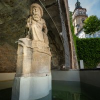Steinfigur am Marktbrunnen in Backnang, darunter Inschrift. Im Hintergrund ein Turm mit Uhr und Fachwerk. Wasserbecken im Vordergrund., &copy; Ren&eacute; Straube