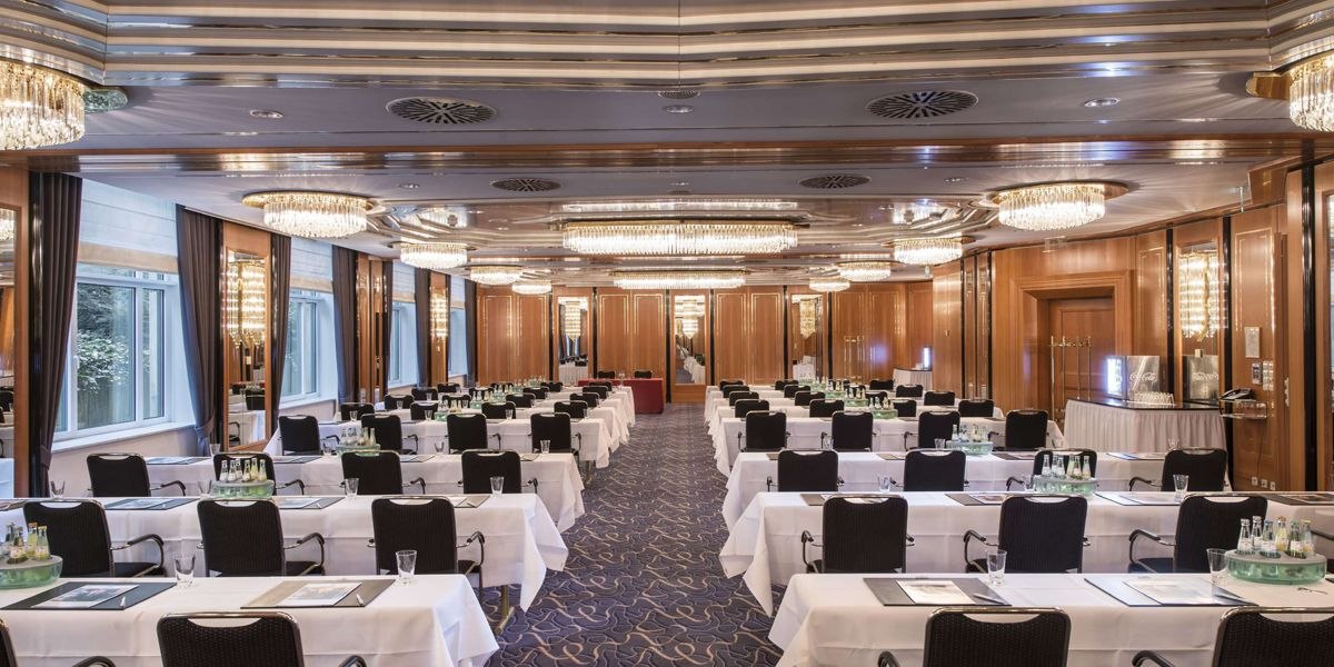 Eleganter Tagungsraum mit weißen Tischdecken, schwarzen Stühlen und Kronleuchtern. Holzwände und große Fenster sorgen für eine stilvolle Atmosphäre., © Maritim Hotelgesellschaft mbH