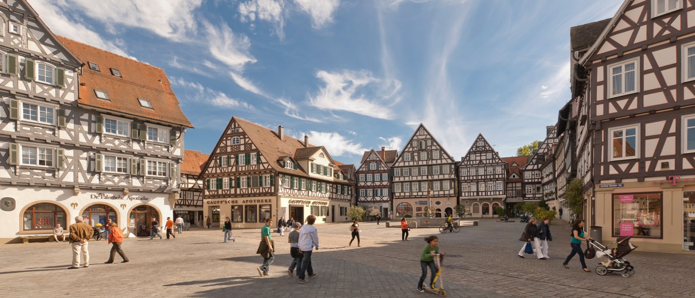 Der Marktplatz in Schorndorf zeigt malerische Fachwerkhäuser unter blauem Himmel. Menschen spazieren und verweilen auf dem Platz., © Oswald