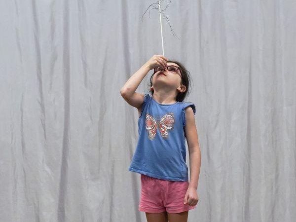 Ein Kind balanciert eine Pfauenfeder auf der Nase. Es trägt ein blaues Shirt mit Schmetterlingsmotiv und rosa Shorts., © Kunstschule Labyrinth