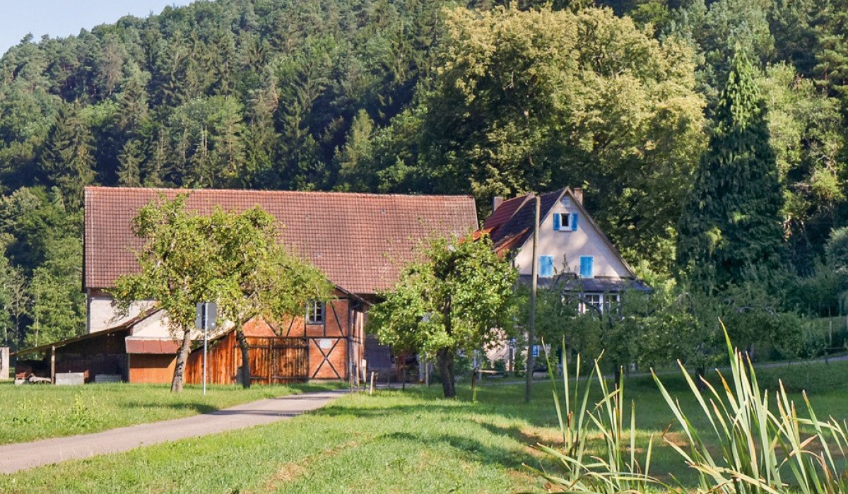 Ein Bauernhof mit Scheune und Wohnhaus, umgeben von Bäumen und Wiesen, vor einem bewaldeten Hügel., © Natur.Nah. Schönbuch & Heckengäu Ein Bauernhof mit Scheune und Wohnhaus, umgeben von Bäumen und Wiesen, vor einem bewaldeten Hügel., © Natur.Nah. Schönbuch & Heckengäu