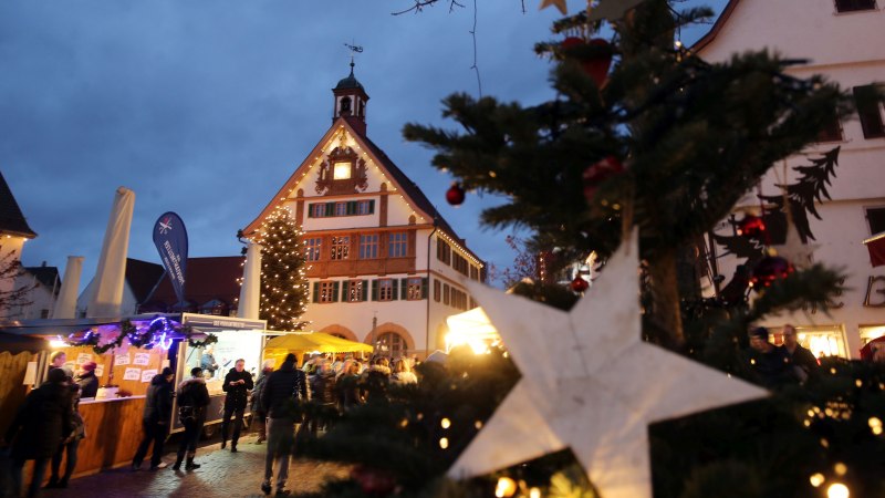 Weihnachtsmarkt in Metzingen: Menschen schlendern zwischen Ständen, ein großer Weihnachtsbaum und ein beleuchtetes Gebäude im Hintergrund., © Stadt Metzingen Weihnachtsmarkt in Metzingen: Menschen schlendern zwischen Ständen, ein großer Weihnachtsbaum und ein beleuchtetes Gebäude im Hintergrund., © Stadt Metzingen