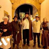 Fünf Personen in historischen Kostümen stehen unter einem beleuchteten Torbogen. Sie tragen Hüte, Umhänge und halten Laternen und Stäbe., © Stadt Winnenden