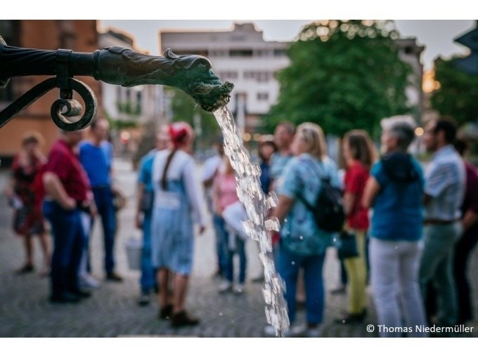 Wasser flie&szlig;t aus einem Brunnenrohr, w&auml;hrend im Hintergrund eine Gruppe von Menschen steht. Die Szene wirkt lebendig und gesellig., &copy; Stuttgart Marketing GmbH