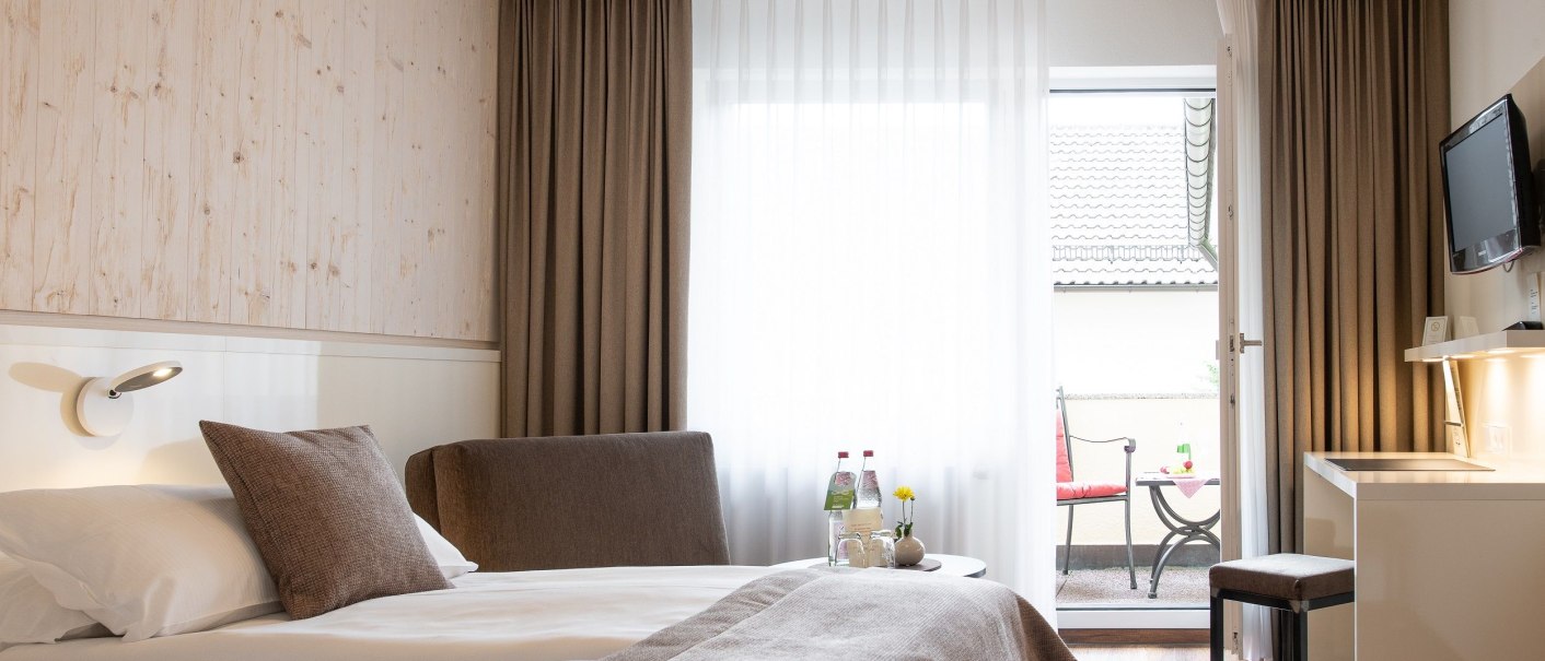 Modernes Hotelzimmer mit Doppelbett, Schreibtisch, Fernseher und Balkon. Dezente Farben und stilvolle Einrichtung schaffen eine gemütliche Atmosphäre., © Hotel Weinstadt