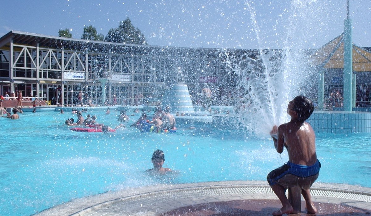 Kinder spielen in einem Freibad. Ein Junge sitzt bei einer Wasserfontäne, während andere im Wasser schwimmen. Im Hintergrund ist ein Gebäude zu sehen., © Natur.Nah. Schönbuch & Heckengäu Kinder spielen in einem Freibad. Ein Junge sitzt bei einer Wasserfontäne, während andere im Wasser schwimmen. Im Hintergrund ist ein Gebäude zu sehen., © Natur.Nah. Schönbuch & Heckengäu