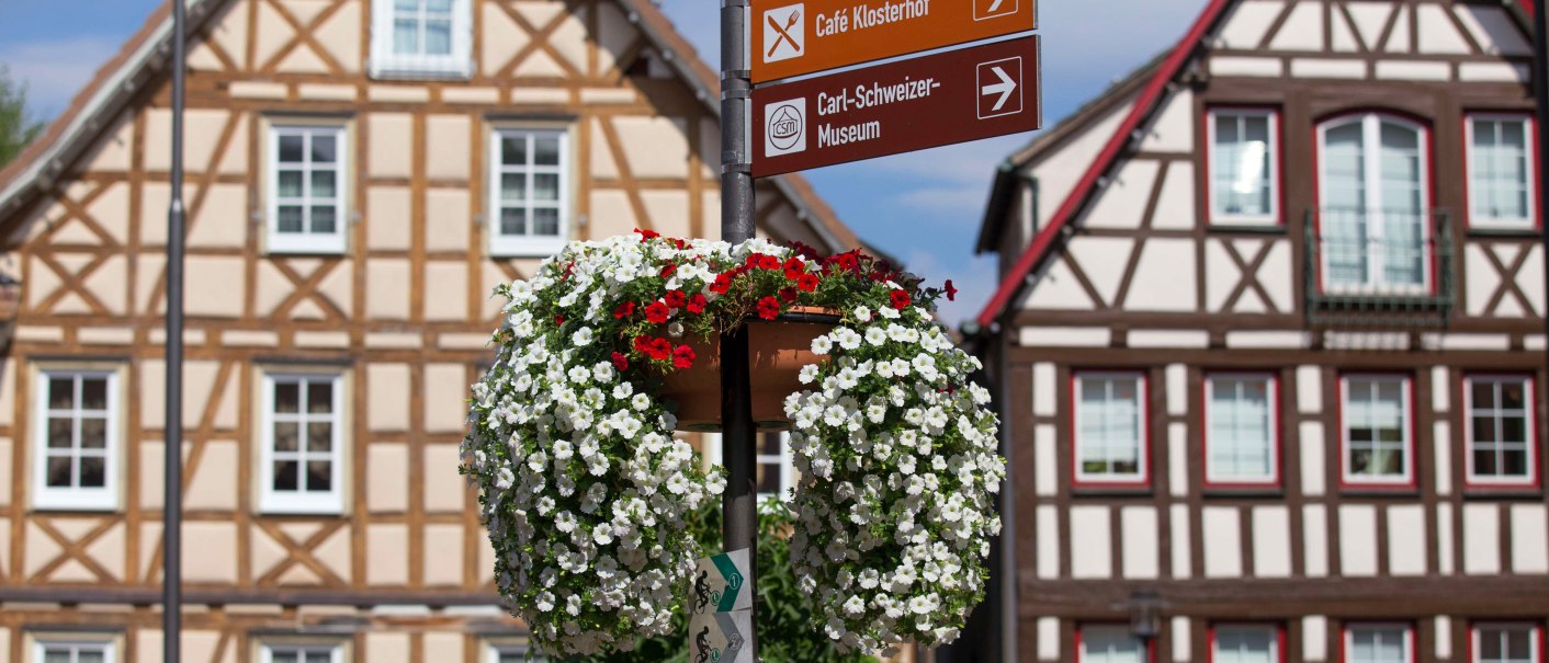 Fachwerkhäuser auf dem Marktplatz von Murrhardt mit einem Wegweiser und blühendem Blumenschmuck im Vordergrund., © Stuttgart-Marketing GmbH, Achim Mende