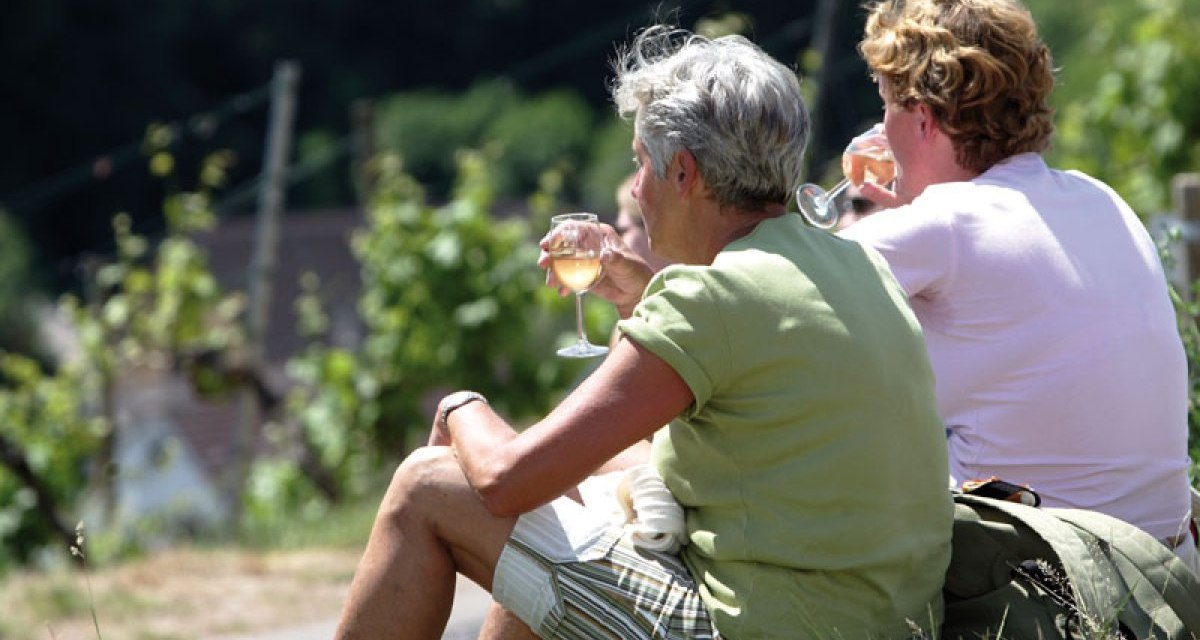 Zwei Personen sitzen im Gras und genießen ein Glas Wein auf einem Weinwanderweg. Im Hintergrund sind Weinreben zu sehen., © Stuttgart-Marketing GmbH Zwei Personen sitzen im Gras und genießen ein Glas Wein auf einem Weinwanderweg. Im Hintergrund sind Weinreben zu sehen., © Stuttgart-Marketing GmbH