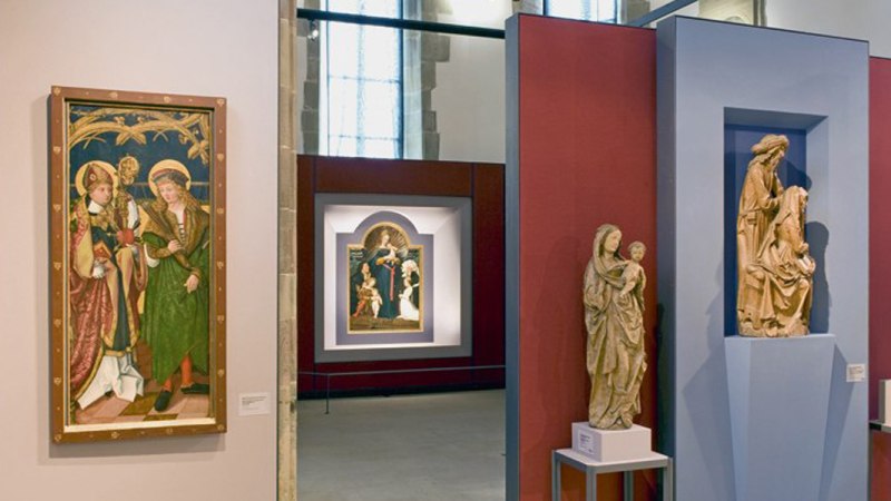 Innenansicht der Johanniterkirche Schwäbisch Hall mit Gemälden und Skulpturen auf roten und blauen Wänden ausgestellt., © Andi Schmid Innenansicht der Johanniterkirche Schwäbisch Hall mit Gemälden und Skulpturen auf roten und blauen Wänden ausgestellt., © Andi Schmid