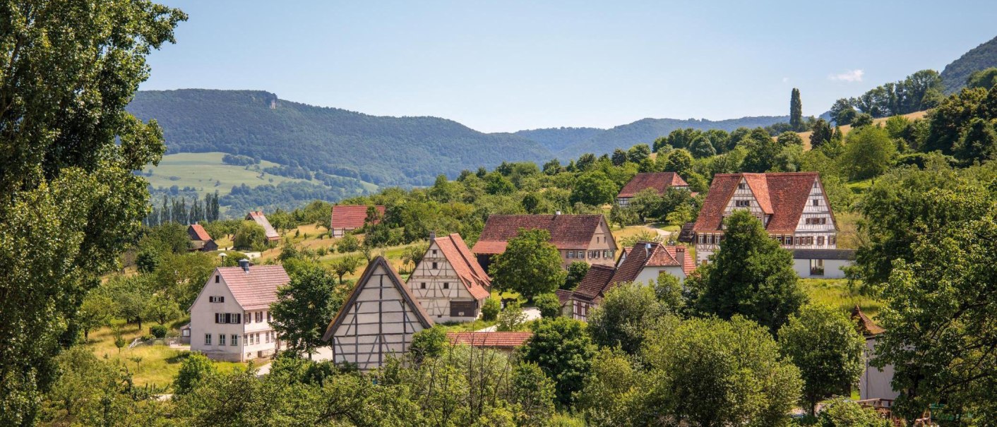 Ein malerisches Dorf mit traditionellen Fachwerkh&auml;usern, umgeben von gr&uuml;nen H&uuml;geln und B&auml;umen, unter einem klaren blauen Himmel., &copy; SMG, Achim Mende