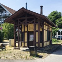 Kleines Fachwerkgebäude am Neckartalradweg, umgeben von Bäumen und einem modernen Gebäude. Ein Infopunkt mit Schildern und Fahrradständer., © J. Tubolzer Kleines Fachwerkgebäude am Neckartalradweg, umgeben von Bäumen und einem modernen Gebäude. Ein Infopunkt mit Schildern und Fahrradständer., © J. Tubolzer