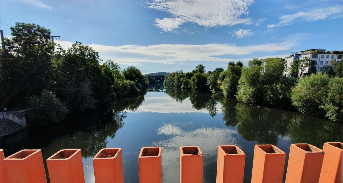 Blick von der Ottosteg-Brücke in Plochingen auf einen ruhigen Fluss, umgeben von Bäumen und Gebäuden, unter einem klaren blauen Himmel., © Kulturamt Plochingen Blick von der Ottosteg-Brücke in Plochingen auf einen ruhigen Fluss, umgeben von Bäumen und Gebäuden, unter einem klaren blauen Himmel., © Kulturamt Plochingen