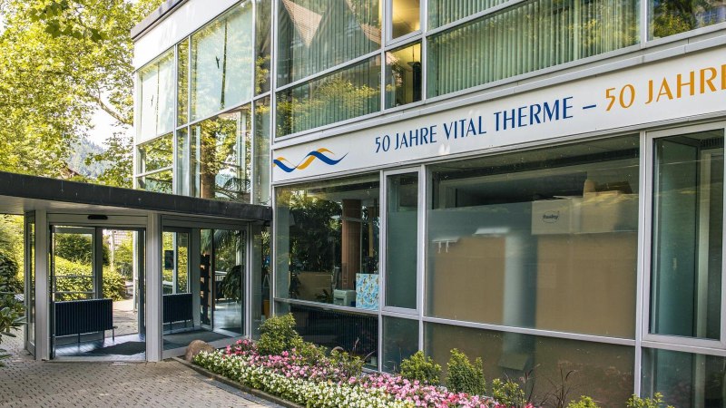 Eingang der Vital Therme mit moderner Glasfassade, umgeben von grünen Bäumen und einem gepflegten Blumenbeet. Ein Schild feiert 50 Jahre Vital Therme., © Stuttgart-Marketing GmbH, Sarah Schmid Eingang der Vital Therme mit moderner Glasfassade, umgeben von grünen Bäumen und einem gepflegten Blumenbeet. Ein Schild feiert 50 Jahre Vital Therme., © Stuttgart-Marketing GmbH, Sarah Schmid