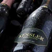 Nahaufnahme von Kessler Sektflaschen, die mit Wassertropfen bedeckt sind. Die Etiketten zeigen verschiedene Sorten wie Rosé und Chardonnay Brut., © none Nahaufnahme von Kessler Sektflaschen, die mit Wassertropfen bedeckt sind. Die Etiketten zeigen verschiedene Sorten wie Rosé und Chardonnay Brut., © none