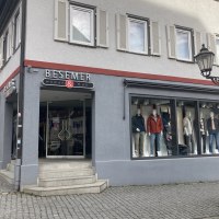Modehaus Besemer in Nürtingen mit Schaufensterpuppen und Eingangstür. Graue Fassade mit roten Akzenten, Kopfsteinpflaster davor., © Lena Besemer Modehaus Besemer in Nürtingen mit Schaufensterpuppen und Eingangstür. Graue Fassade mit roten Akzenten, Kopfsteinpflaster davor., © Lena Besemer