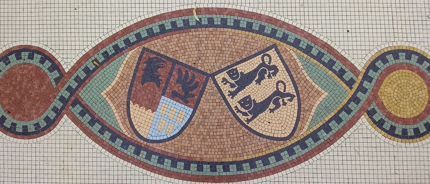Mosaik des Allianzwappen von Graf Gottfried vonP&uuml;ckler-Gaildorf und Gr&auml;fin Adele von Hohenlohe-Ingelfingen.Die Wappenschilde sind umgeben von dekorativen Mustern in Rot, Gr&uuml;n, Schwarz und Gelb., &copy; Petra Natzkowski