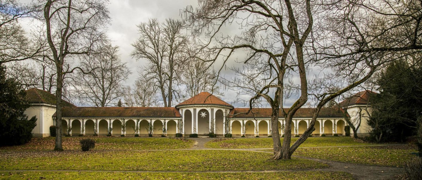 Historisches Kurhaus in Bad Boll mit Arkaden, umgeben von kahlen Bäumen und einem grünen Rasen im Vordergrund., © Stuttgart-Marketing GmbH, Sarah Schmid Historisches Kurhaus in Bad Boll mit Arkaden, umgeben von kahlen Bäumen und einem grünen Rasen im Vordergrund., © Stuttgart-Marketing GmbH, Sarah Schmid