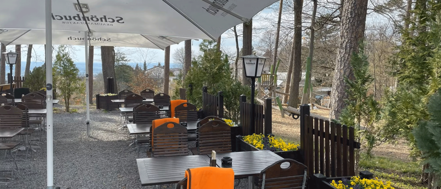 Ein ruhiger Biergarten mit Holztischen und -stühlen, umgeben von Bäumen. Große Sonnenschirme spenden Schatten, gelbe Blumen schmücken den Bereich., © Schönbuch Waldbiergarten am Wasserturm Ein ruhiger Biergarten mit Holztischen und -stühlen, umgeben von Bäumen. Große Sonnenschirme spenden Schatten, gelbe Blumen schmücken den Bereich., © Schönbuch Waldbiergarten am Wasserturm