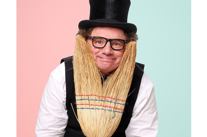 Ein Mann mit Zylinder und Brille posiert mit einem Besen, der wie ein Bart aussieht, vor einem zweifarbigen Hintergrund., © Stadt Murrhardt
