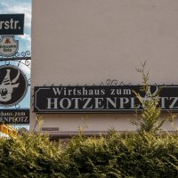 Schild des Wirtshauses zum Hotzenplotz an der Lindensp&uuml;rstra&szlig;e, umgeben von gr&uuml;nen B&uuml;schen und einem blauen Himmel im Hintergrund., &copy; SMG. Sarah Schmid