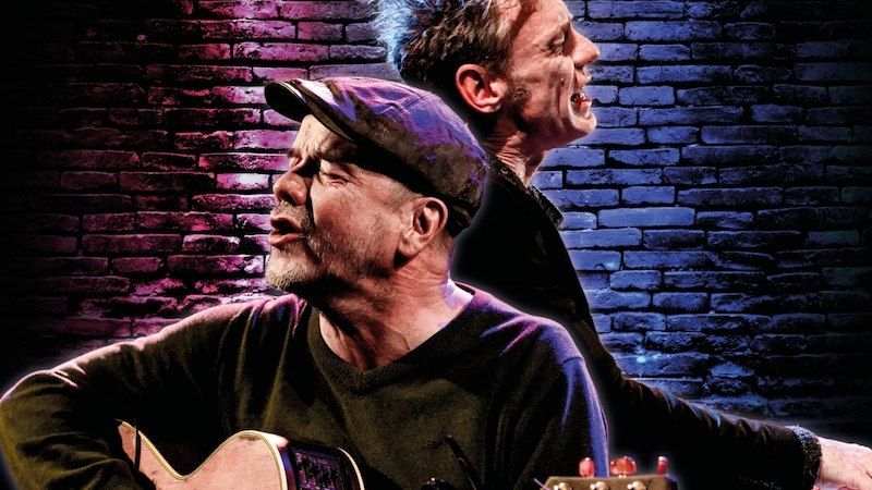 Zwei Musiker performen leidenschaftlich auf einer Bühne, einer mit Gitarre, der andere am Keyboard, vor einer beleuchteten Backsteinwand., © Kulturhaus Schwanen