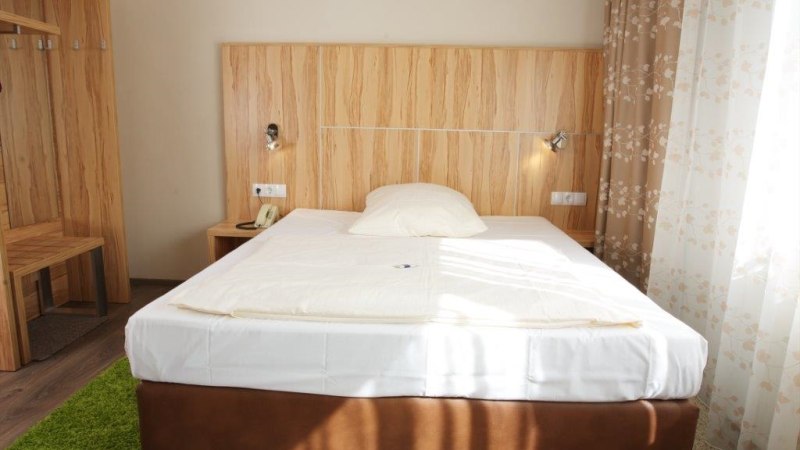 Ein gemütliches Einzelzimmer mit einem Bett, Holzmöbeln und floralen Vorhängen. Ein grüner Teppich liegt auf dem Boden., © Hotel Reinhardtshof Garni Ein gemütliches Einzelzimmer mit einem Bett, Holzmöbeln und floralen Vorhängen. Ein grüner Teppich liegt auf dem Boden., © Hotel Reinhardtshof Garni