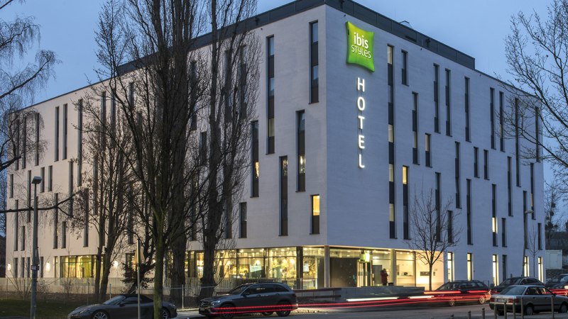Modernes Hotelgeb&auml;ude des ibis Styles Stuttgart Vaihingen bei D&auml;mmerung, beleuchtet mit Autos auf der Stra&szlig;e davor., &copy; ibis Styles Stuttgart Vaihingen