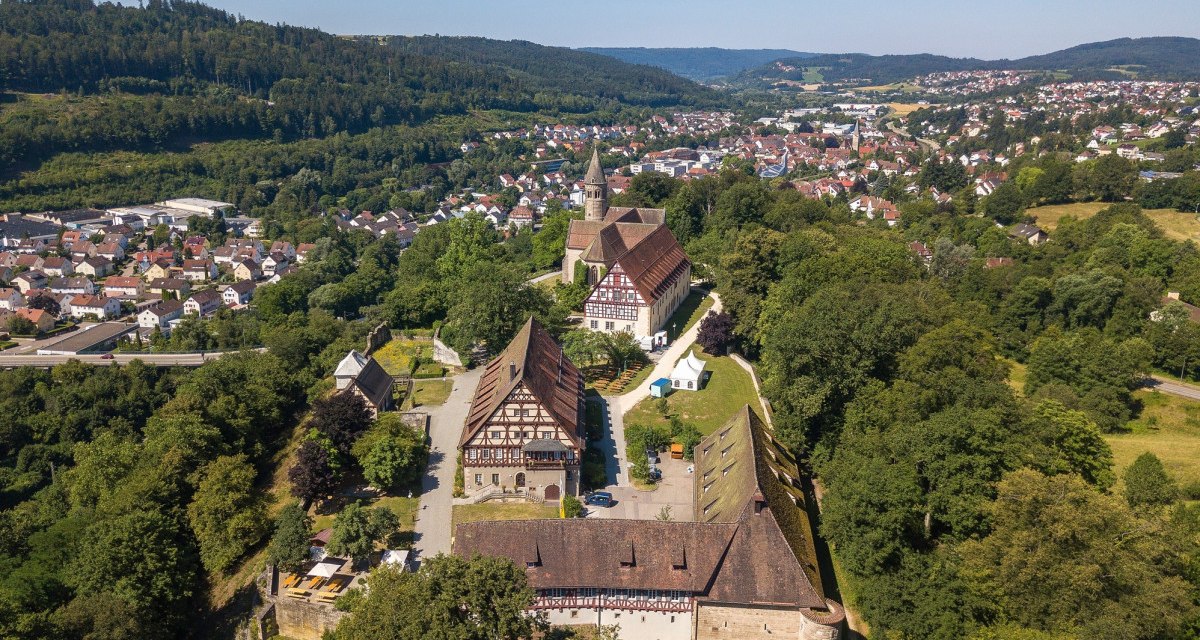 Luftaufnahme des Klosters Lorch, umgeben von Bäumen und einer kleinen Stadt im Hintergrund. Historische Gebäude und eine Kirche sind sichtbar., © Remstal Tourismus e.V.