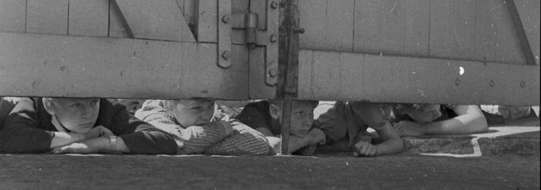 Mehrere Kinder liegen auf dem Boden und schauen neugierig unter einem gro&szlig;en Holztor hindurch., &copy; Staatsarchiv Ludwigsburg