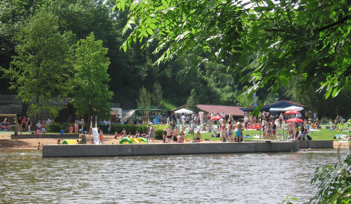 Menschen im Kocherfreibad Künzelsau genießen einen sonnigen Tag. Im Vordergrund Wasser, im Hintergrund Bäume und eine Wiese mit Badegästen., © Touristikgemeinschaft Hohenlohe, Künzelsau / Stadt Künzelsau Menschen im Kocherfreibad Künzelsau genießen einen sonnigen Tag. Im Vordergrund Wasser, im Hintergrund Bäume und eine Wiese mit Badegästen., © Touristikgemeinschaft Hohenlohe, Künzelsau / Stadt Künzelsau