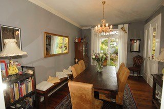 Esszimmer mit langem Holztisch, Stühlen, Kronleuchter, Spiegel und Bücherregal. Helle Vorhänge und Blumen auf dem Tisch., © Elsbeth Koch Esszimmer mit langem Holztisch, Stühlen, Kronleuchter, Spiegel und Bücherregal. Helle Vorhänge und Blumen auf dem Tisch., © Elsbeth Koch