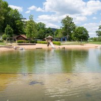 Das Kocherfreibad in Künzelsau zeigt einen Sandstrand, einen Spielplatz mit Rutsche und Schaukeln, umgeben von Bäumen und einem klaren Himmel., © Olivier Schniepp, Foto Linke GmbH