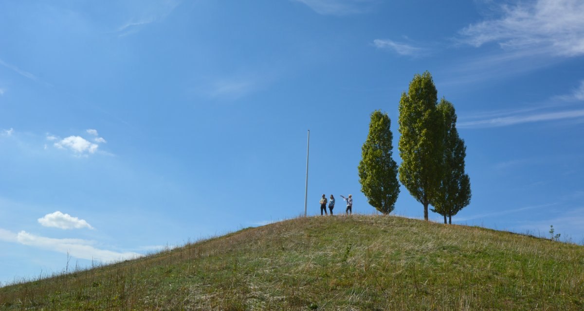 Drei Personen stehen auf einem grasbewachsenen Hügel neben zwei Bäumen und einem Fahnenmast unter klarem, blauem Himmel., © Remstal Tourismus e.V. Drei Personen stehen auf einem grasbewachsenen Hügel neben zwei Bäumen und einem Fahnenmast unter klarem, blauem Himmel., © Remstal Tourismus e.V.
