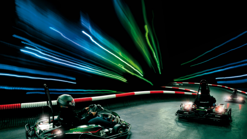 Zwei Karts fahren auf einer beleuchteten Indoor-Strecke. Lichtstreifen in Blau und Gr&uuml;n erzeugen einen dynamischen Effekt., &copy; Sensapolis Sindelfingen