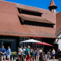 Besucher stehen vor dem Weinbaumuseum in Uhlbach. Das Fachwerkgebäude hat ein rotes Ziegeldach. Im Hintergrund sind Weinberge zu sehen., © Stuttgart-Marketing GmbH, Thomas Niedermüller