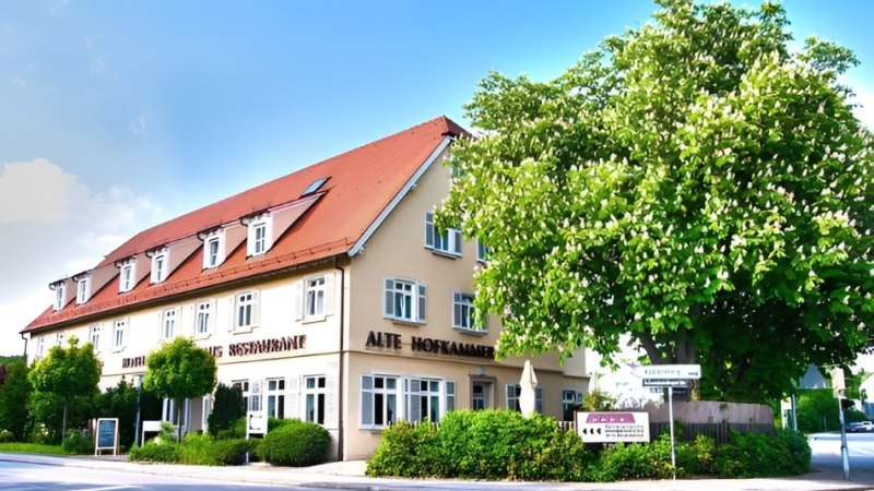 Ein Hotel mit rotem Dach und mehreren Fenstern, umgeben von Bäumen und Büschen, unter blauem Himmel., © Hotel Neuwirtshaus Ein Hotel mit rotem Dach und mehreren Fenstern, umgeben von Bäumen und Büschen, unter blauem Himmel., © Hotel Neuwirtshaus