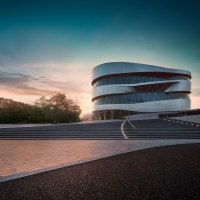 Das Mercedes-Benz Museum in Stuttgart bei Sonnenuntergang. Moderne Architektur mit geschwungenen Linien, umgeben von Bäumen und beleuchteten Stufen., © Mercedes-Benz Heritage GmbH Das Mercedes-Benz Museum in Stuttgart bei Sonnenuntergang. Moderne Architektur mit geschwungenen Linien, umgeben von Bäumen und beleuchteten Stufen., © Mercedes-Benz Heritage GmbH