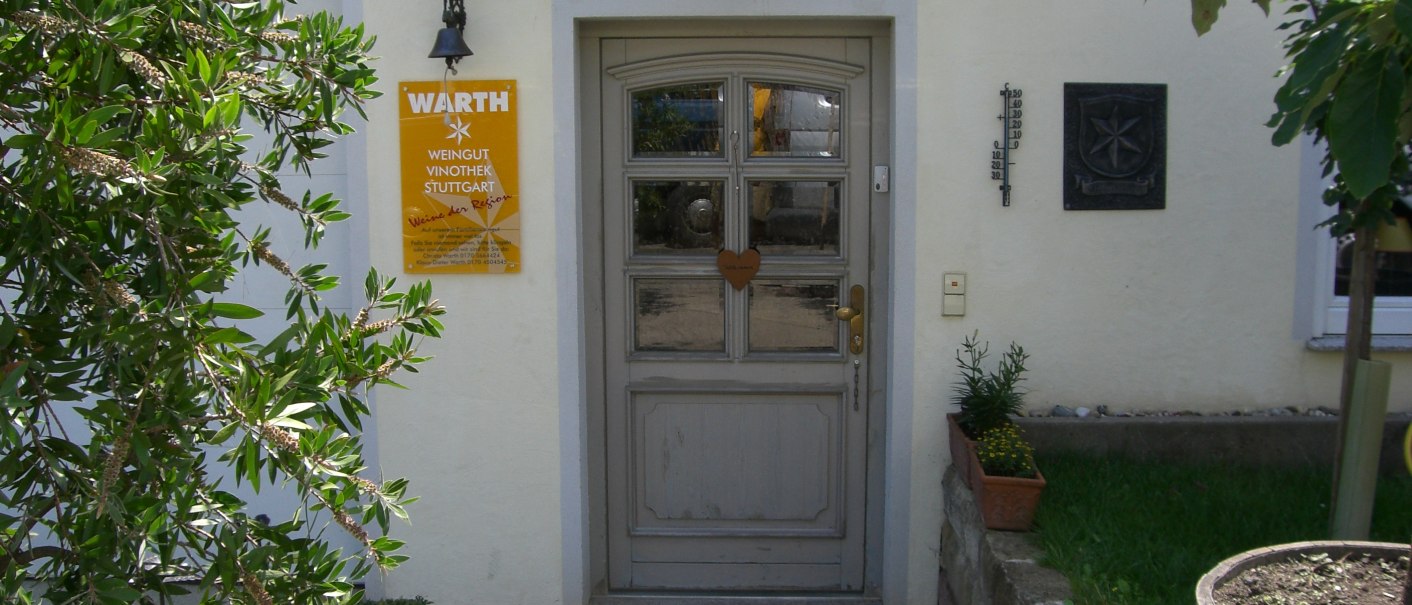 Eingang des Weinguts Warth mit gelbem Schild, Pflanzen und Holztür. Ein Thermometer und ein Wappen sind an der Wand angebracht., © Weingut Warth