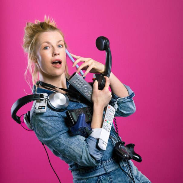 Frau in Jeansjacke hält viele elektronische Geräte wie Fernbedienungen und Kopfhörer vor einem pinken Hintergrund., © Mauerwerk GmbH Frau in Jeansjacke hält viele elektronische Geräte wie Fernbedienungen und Kopfhörer vor einem pinken Hintergrund., © Mauerwerk GmbH