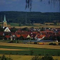 Ein Dorf mit roten Dächern und einer Kirche mit grünem Turm, umgeben von Feldern und Hügeln im Hintergrund., © http://www.renningen.de/index.php?id=574 Ein Dorf mit roten Dächern und einer Kirche mit grünem Turm, umgeben von Feldern und Hügeln im Hintergrund., © http://www.renningen.de/index.php?id=574