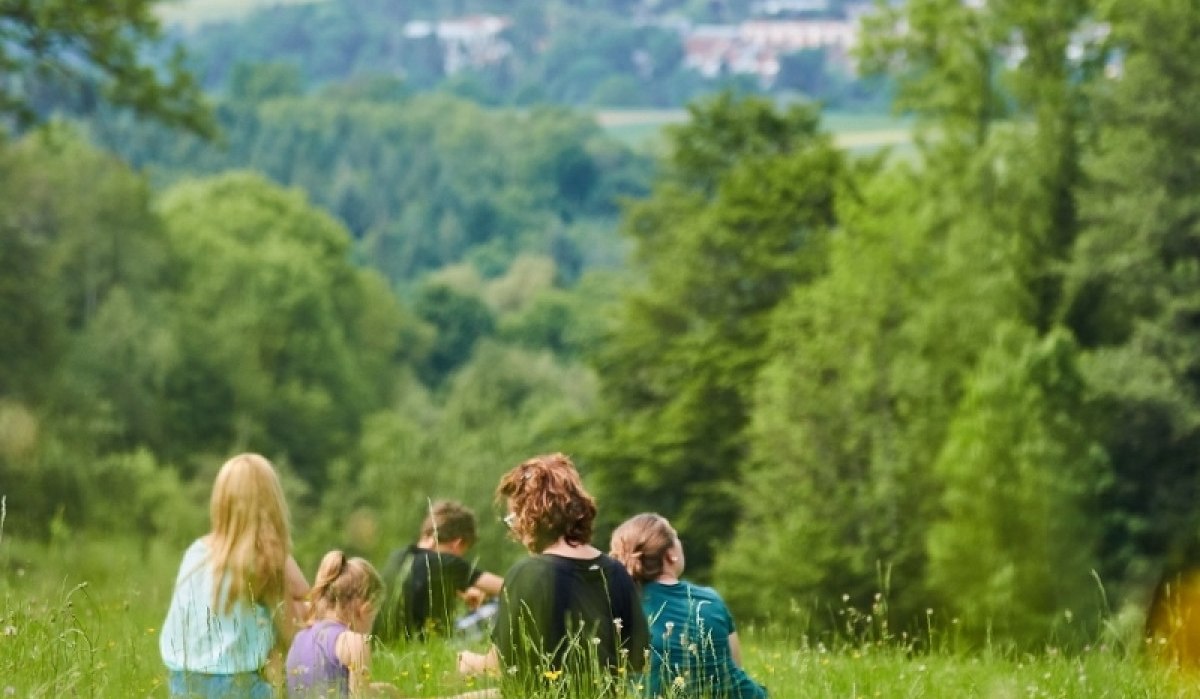 Gruppe von Menschen sitzt auf einer grünen Wiese, umgeben von Bäumen, mit Blick auf ein Dorf in der Ferne., © Natur.Nah. Schönbuch & Heckengäu