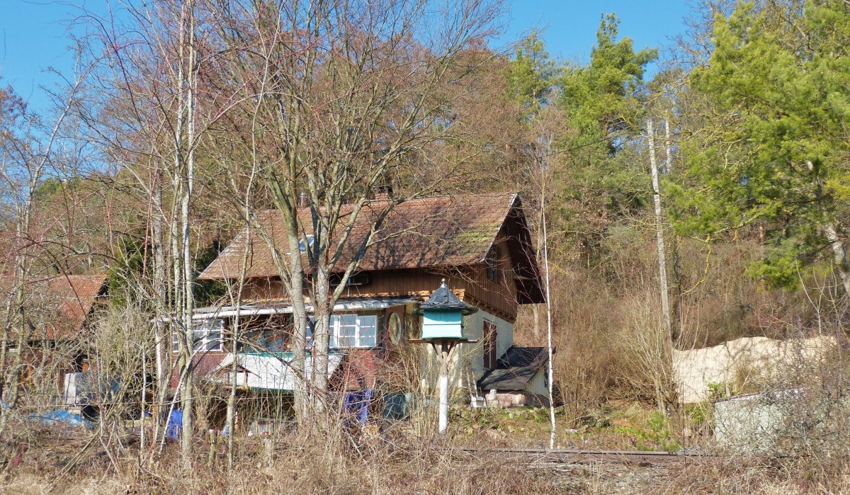 Ein ehemaliges Bahnw&auml;rterhaus steht inmitten von B&auml;umen und Str&auml;uchern. Das Geb&auml;ude hat ein schr&auml;ges Dach und ist von Natur umgeben., &copy; Natur.Nah. Sch&ouml;nbuch & Heckeng&auml;u