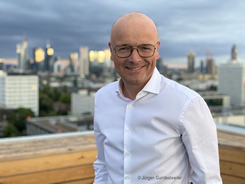 Ein Mann mit Brille und wei&szlig;em Hemd steht l&auml;chelnd auf einer Dachterrasse. Im Hintergrund ist eine Stadt mit Hochh&auml;usern zu sehen., &copy; Stadthalle Leonberg